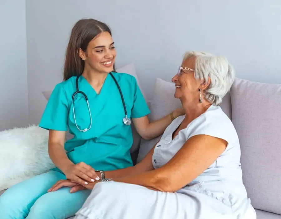 Home health nurse speaking with elderly client on couch in home